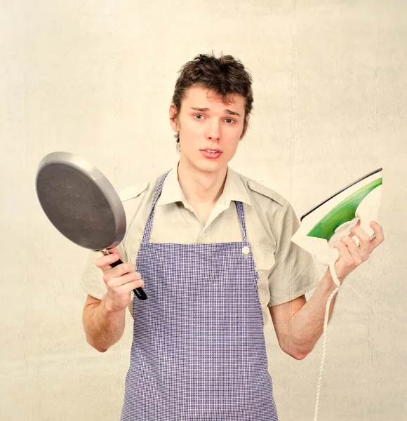 Young man wearing apron and holding pan and iron — Stock Photo, Image