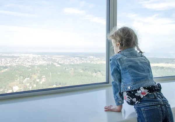 Liten flicka tittar genom fönstret på skyskrapa — Stockfoto