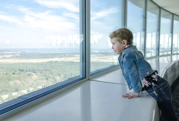 Little girl looking through the window at skyscraper — Stock Photo, Image