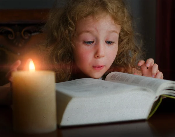 Schattig klein meisje, zittend in het donker met brandende kaars en lezen van een boek — Stockfoto