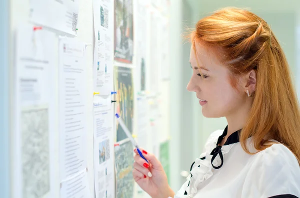 Young female student looking through job offers on board — Stock Photo, Image