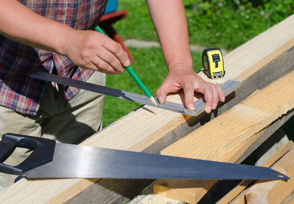 Manos masculinas que miden y marcan tablón de madera al aire libre — Foto de Stock