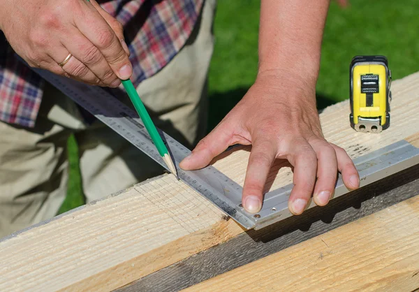 Male hands measuring and marking wooden plank outdoors — Stock Photo, Image