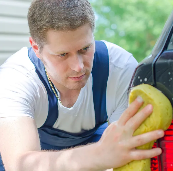 Junger Arbeiter wäscht Auto mit gelbem Schwamm — Stockfoto