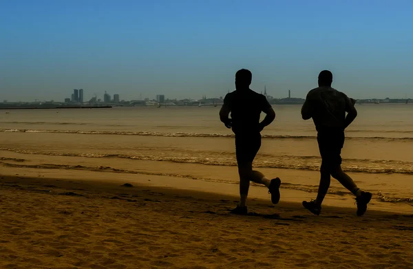 Rara vista de la silueta de dos hombres corriendo en la orilla del mar —  Fotos de Stock