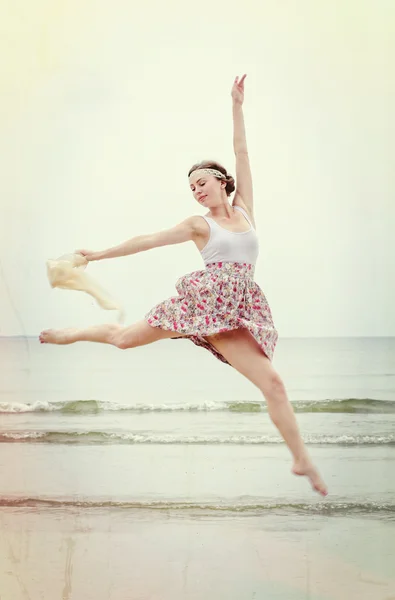 Jeune femme en saut avec écharpe sur un rivage — Photo