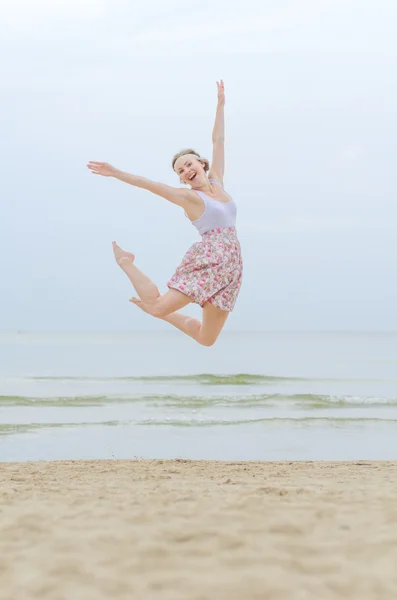 Joven mujer feliz saltando en una orilla del mar — Foto de Stock