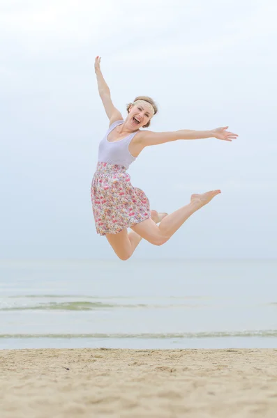 Giovane donna felice che salta su una riva del mare — Foto Stock