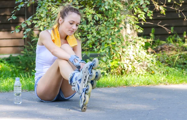 Young female skater sitting on the road and ties her rollers — Stock Photo, Image