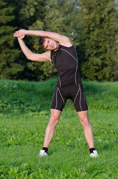 Young sportsman stretching before workout in park — Stock Photo, Image
