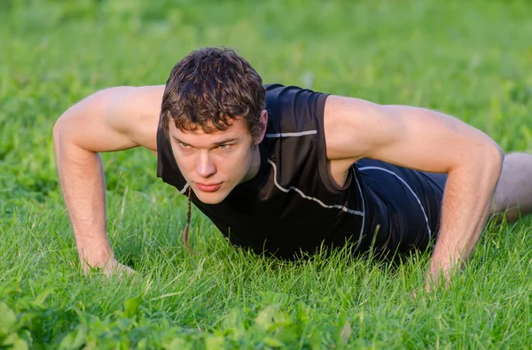 Jóképű férfi csinál fekvőtámaszokat a parkban — Stock Fotó