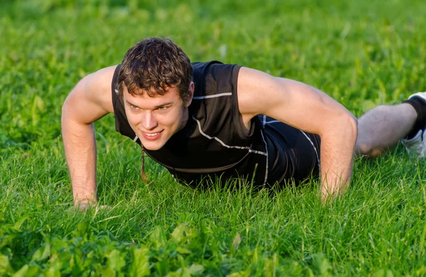 Szép mosolygó ember csinál fekvőtámaszokat a parkban — Stock Fotó