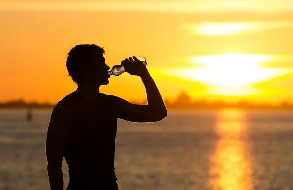 Hombre bebiendo botella de agua en la playa al amanecer — Foto de Stock