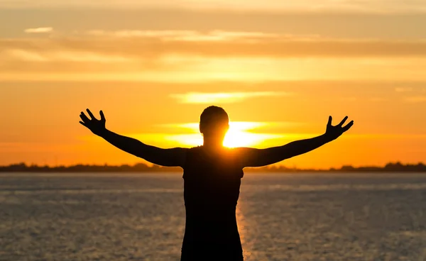 Homem com os braços abertos na praia ao nascer do sol — Fotografia de Stock
