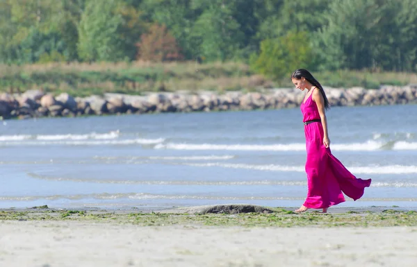 Mujer vestida de rosa caminando por la playa. Lugar para el texto — Foto de Stock