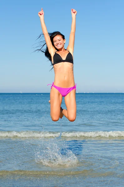 Szczęśliwa kobieta skoki w wodzie na plaży — Zdjęcie stockowe