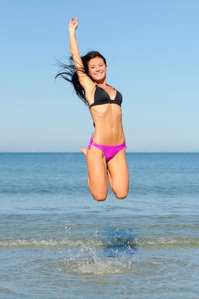Счастливая женщина прыгает в воду на пляже — стоковое фото