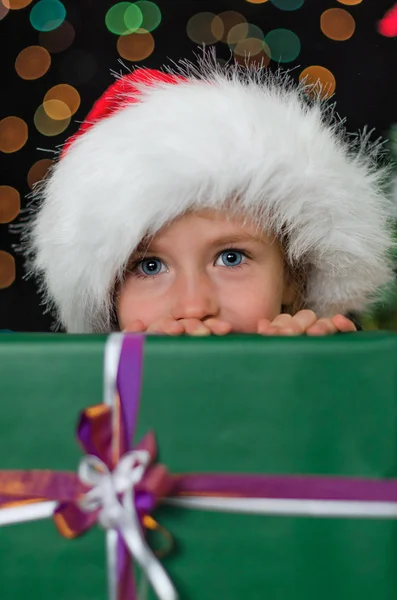 Menina se escondendo atrás de um presente de Natal . — Fotografia de Stock