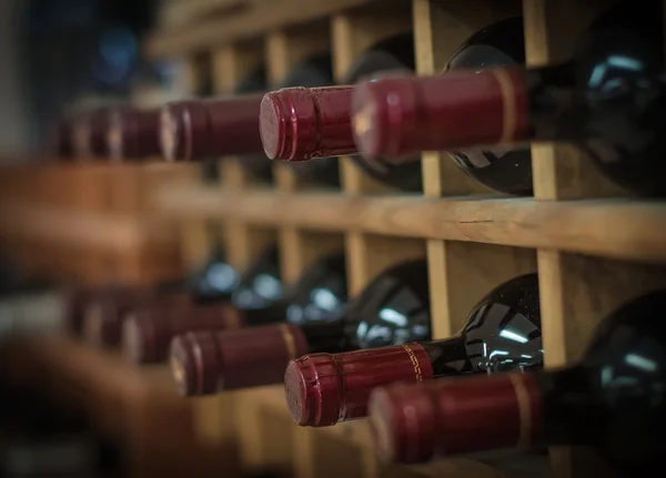 Kırmızı şarap şişelerini ahşap raflar üzerinde yığılmış — Stok fotoğraf