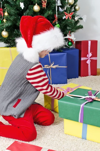 Petite fille dans le chapeau du Père Noël déballer cadeaux de Noël — Photo