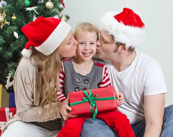 Parents kissing daughter in front of christmas tree. — Stock Photo, Image