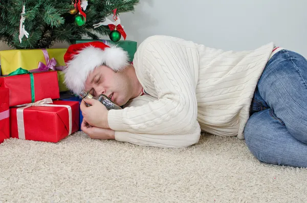Drunk man with bottle sleeps under christmas tree — Stock Photo, Image
