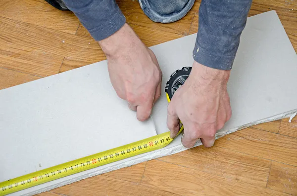 Mains masculines mesurant et coupant le placoplâtre — Photo