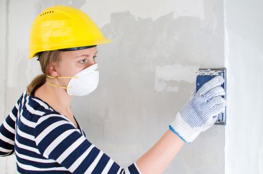 Female plasterer in hard hat polishing the wall. clipart