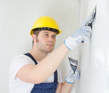 Male builder repairs wall with spackling paste clipart