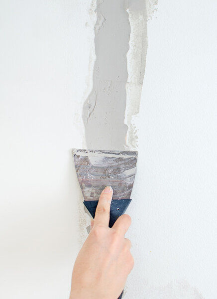 Female hand repairs wall with spackling paste