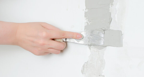 Female hand repairs wall with spackling paste