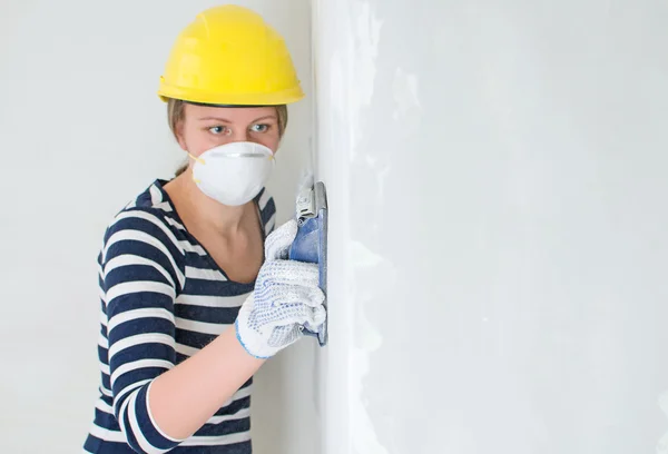 Female plasterer in hard hat polishing the wall. Place for your text. — Stock Photo, Image