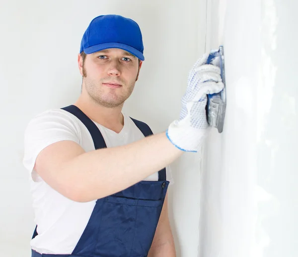 Male plasterer in baseball cap polishing the wall. — Stock Photo, Image
