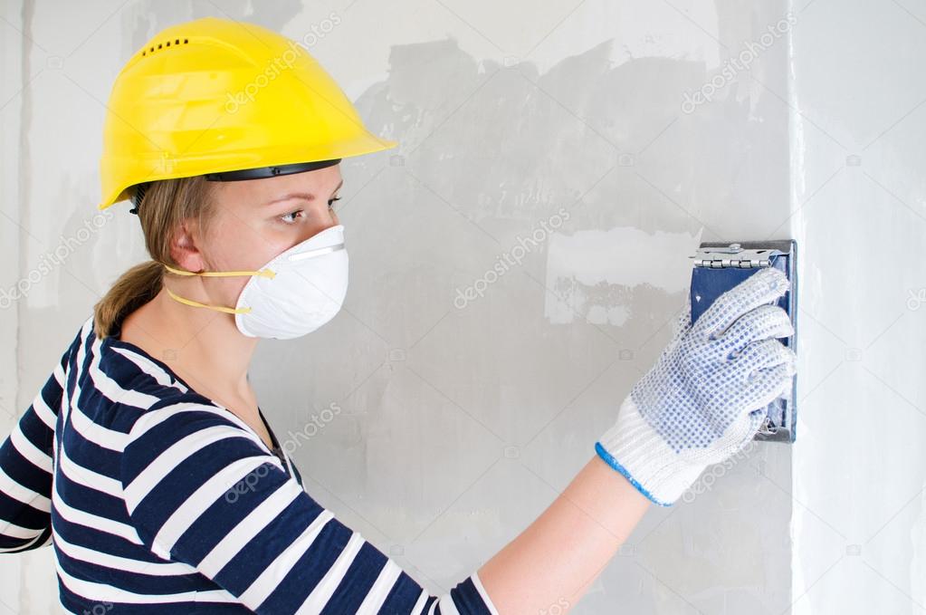 Female plasterer in hard hat polishing the wall.