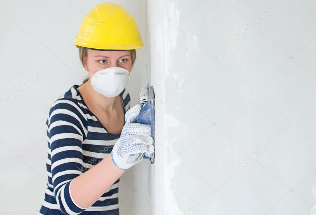 Female plasterer in hard hat polishing the wall. Place for your text.