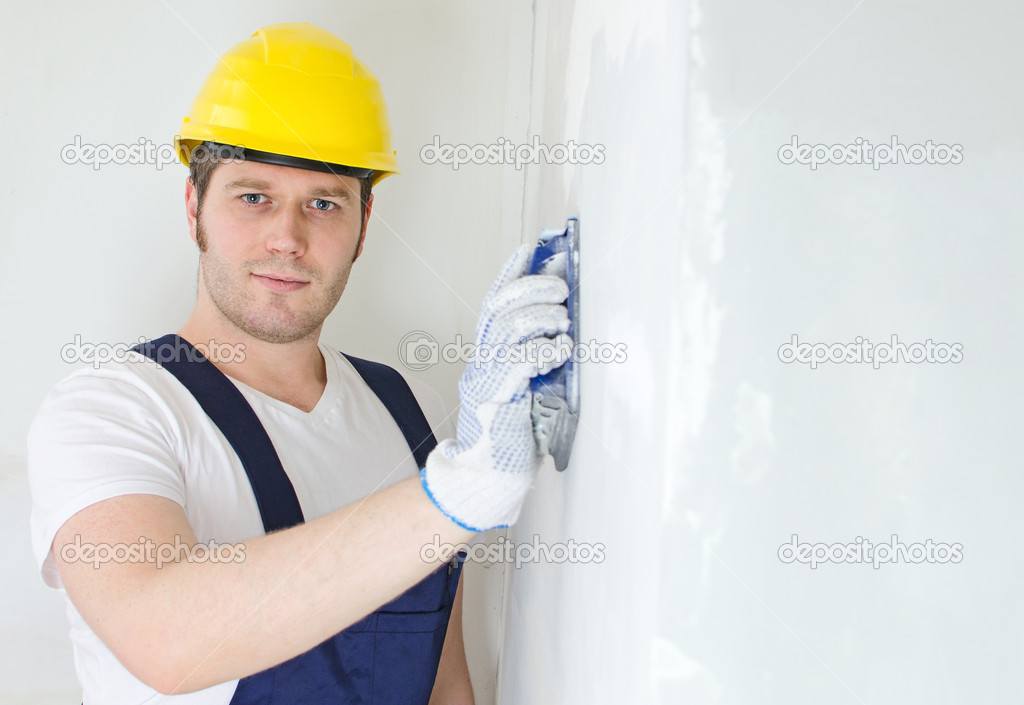 Male plasterer in hard hat polishing the wall. Space for text.