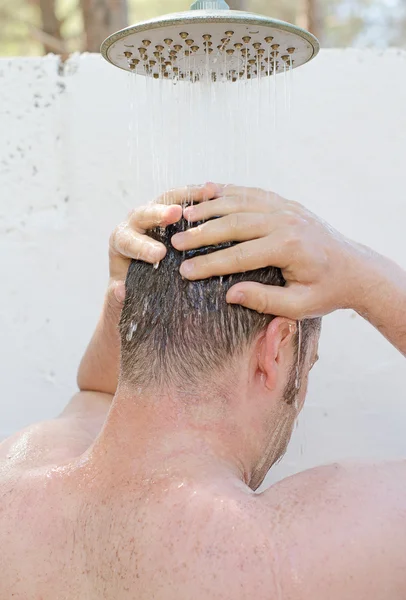 Un hombre duchándose al aire libre. Vista desde atrás . — Foto de Stock