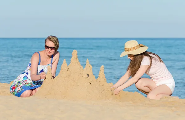 Twee vrienden met zandkasteel op het strand. — Stockfoto