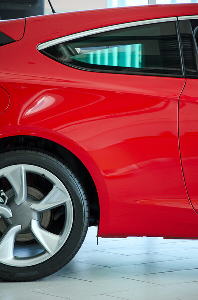 Part of red car at dealership salon.