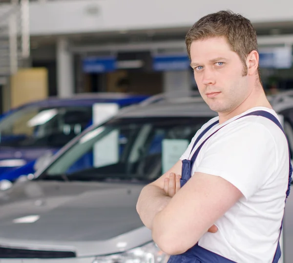 Jovem mecânico bonito na concessionária de automóveis. Lugar para texto . — Fotografia de Stock