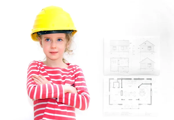 Niña en sombrero duro de pie cerca de la pared con el plan de la casa . — Foto de Stock