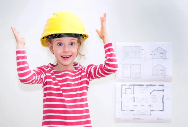 Маленька дівчинка в капелюсі, що стоїть біля стіни з планом будинку . — стокове фото