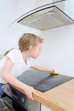 küçük kız cooktop evde mutfakta siliyor..