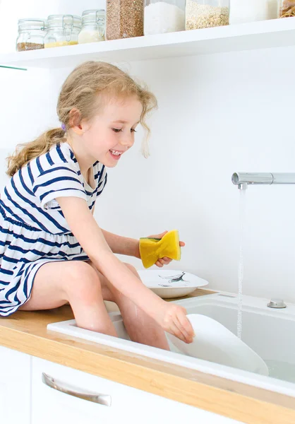 Szczęśliwy dziewczynki mycie naczyń w kuchni. — Zdjęcie stockowe