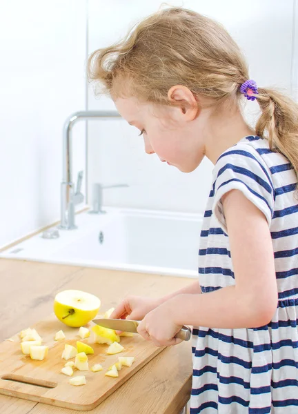 Liten flicka skär äpple i köket. — Stockfoto