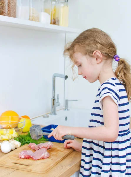 Klein meisje verslaat vlees in de keuken. — Stockfoto