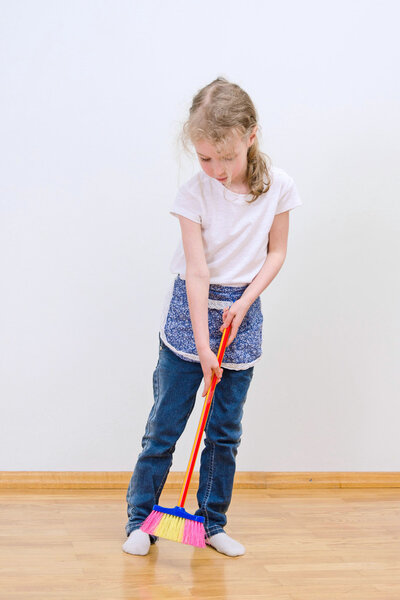 Little cute girl brooming floor at home.