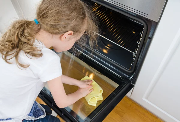 Klein meisje veegt oven in de keuken thuis. — Stockfoto