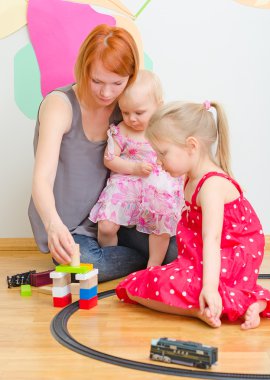 Little girls and mother playing with railway sitting on the floor. clipart