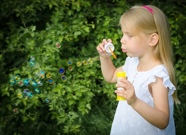 Kleines Mädchen pustet Seifenblasen im Park. — Stockfoto